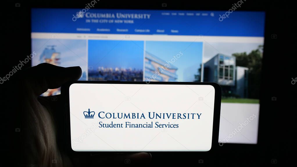 Stuttgart, Germany - 10-09-2025: Person holding cellphone with logo of Columbia University in the City of New York on screen in front of webpage. Focus on phone display.