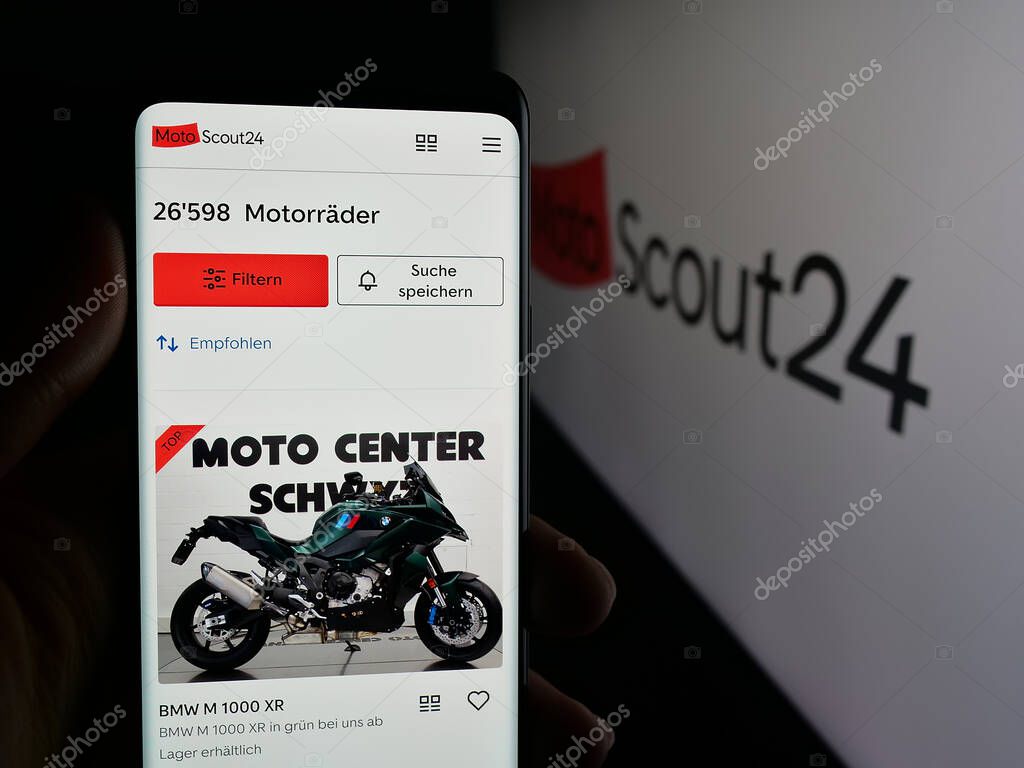 Stuttgart, Germany - 10-09-2025: Person holding cellphone with webpage of motorcycle marketplace company MotoScout24 on screen in front of logo. Focus on center of phone display.