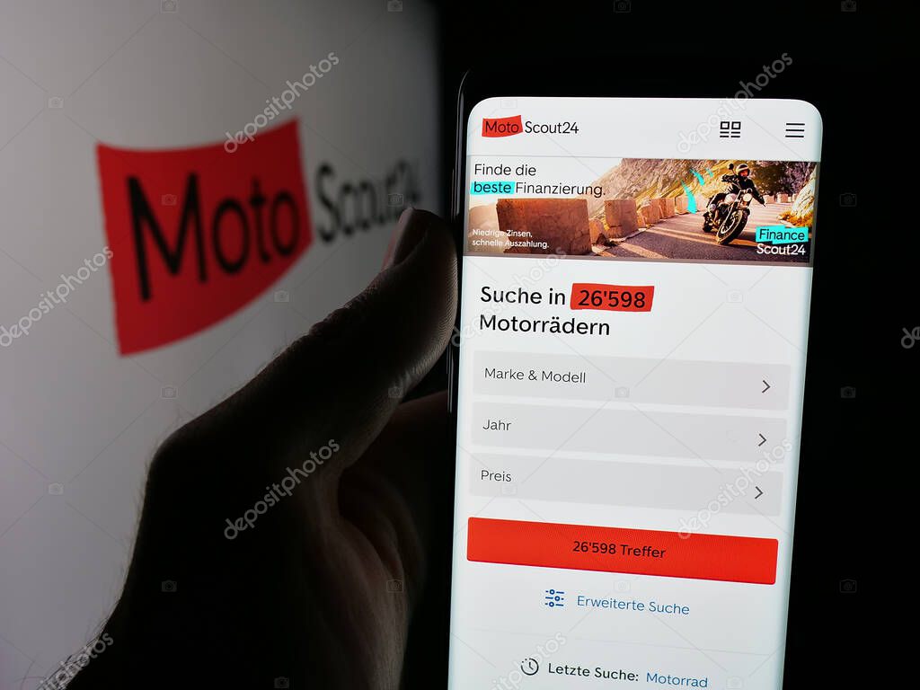 Stuttgart, Germany - 10-09-2025: Person holding smartphone with web page of motorcycle marketplace company MotoScout24 on screen in front of logo. Focus on center of phone display.