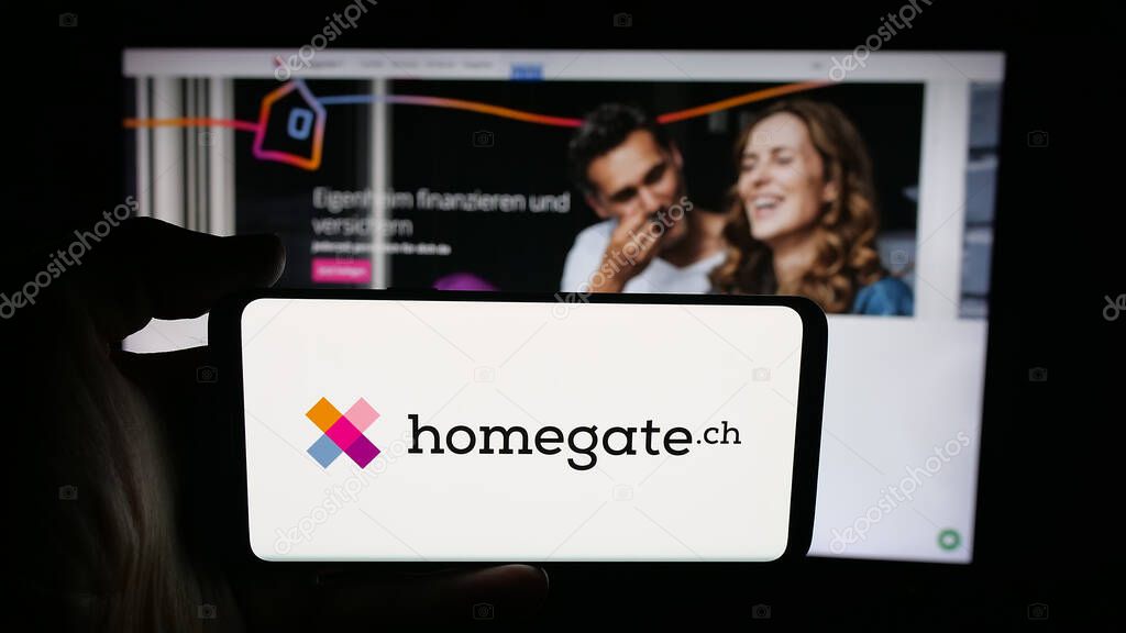 Stuttgart, Germany - 10-09-2025: Person holding cellphone with logo of Swiss real estate portal company Homegate on screen in front of webpage. Focus on phone display.