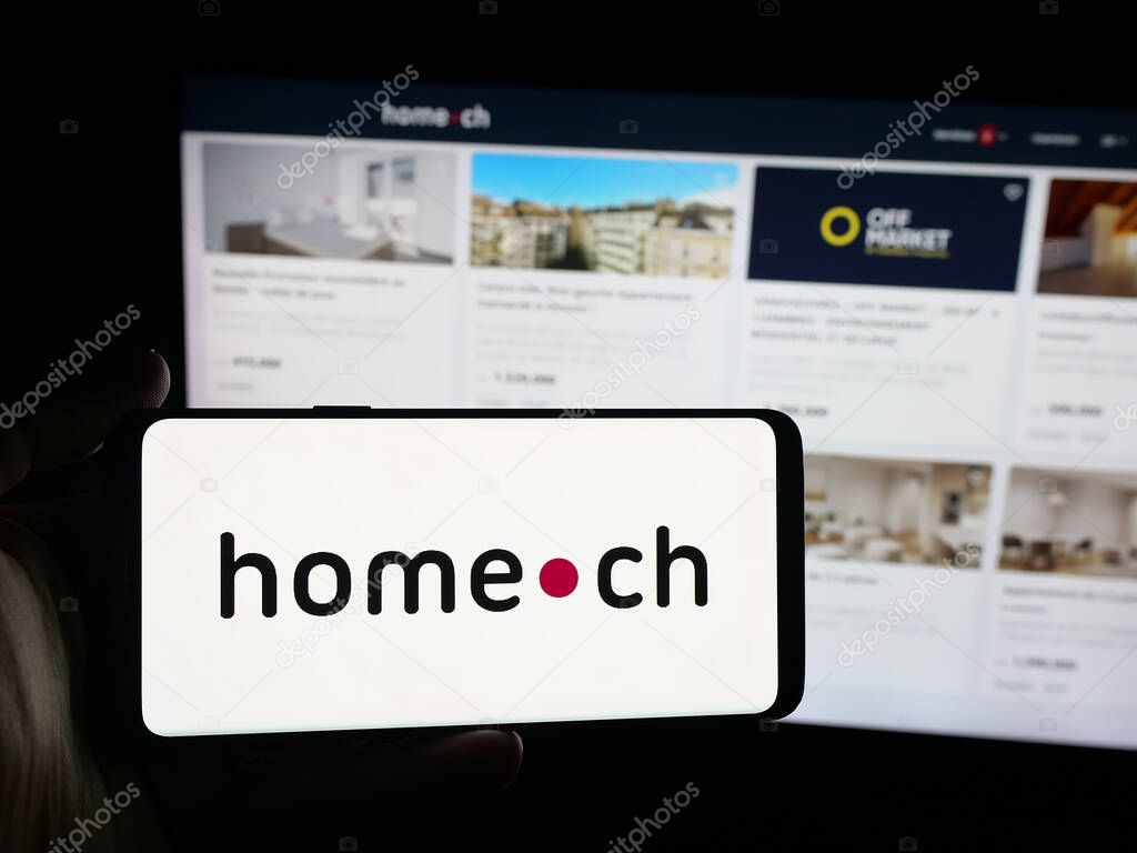 Stuttgart, Germany - 10-09-2025: Person holding smartphone with logo of Swiss real estate portal company Home.ch on screen in front of website. Focus on phone display.