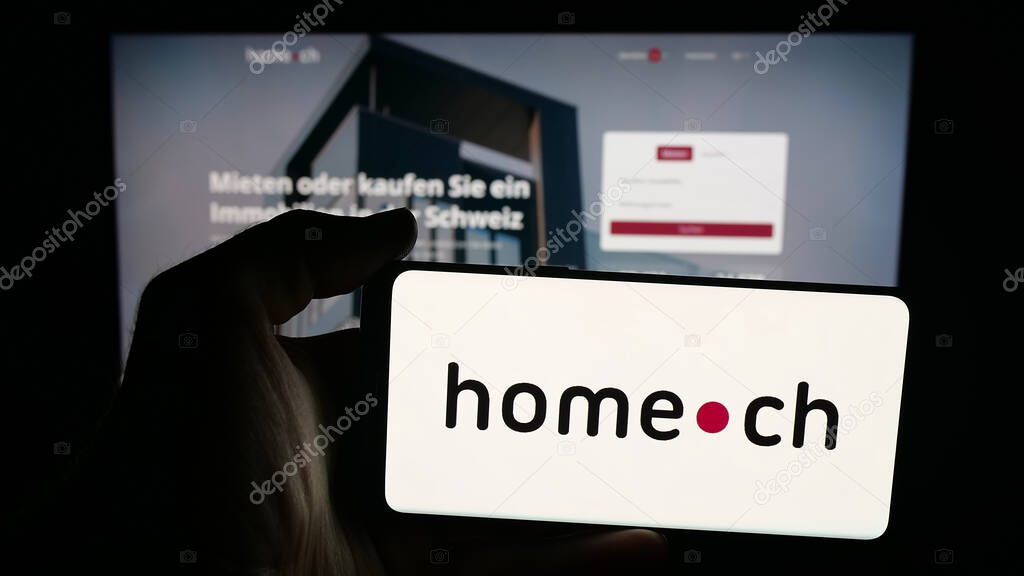 Stuttgart, Germany - 10-09-2025: Person holding mobile phone with logo of Swiss real estate portal company Home.ch on screen in front of web page. Focus on phone display.