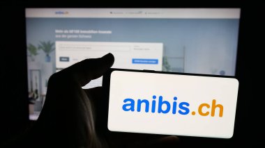 Stuttgart, Almanya - 10-09-2025: Üzerinde İsviçre 'de sınıflandırılmış platform şirketi anibi.ch logosu bulunan cep telefonu sahibi kişi web sayfasının önünde ekranda. Telefon ekranına odaklan.