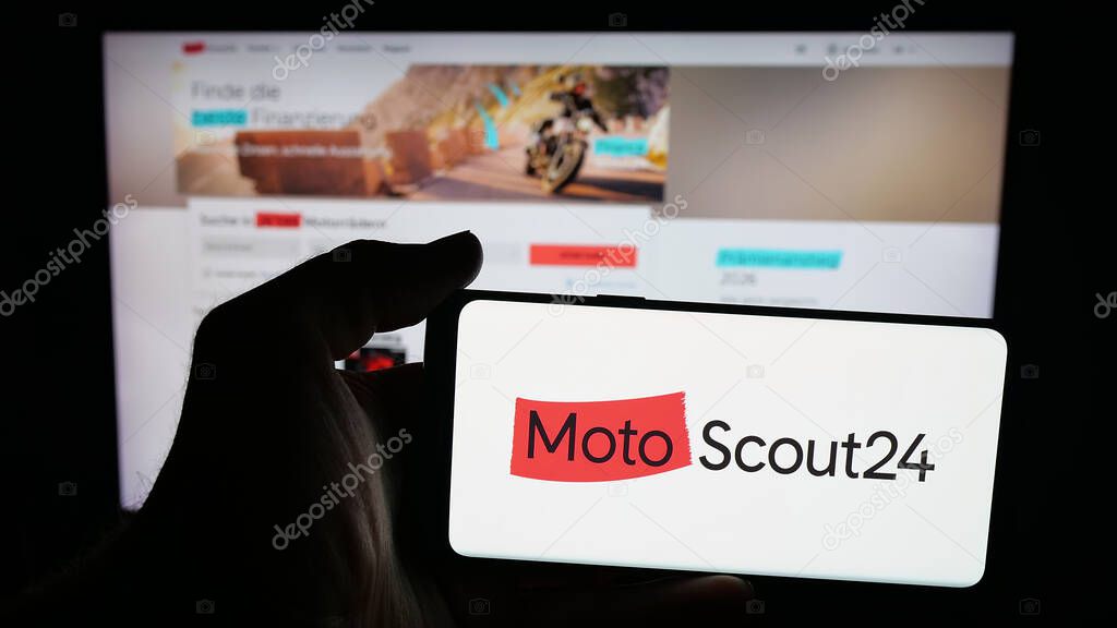 Stuttgart, Germany - 10-09-2025: Person holding mobile phone with logo of motorcycle marketplace company MotoScout24 on screen in front of web page. Focus on phone display.