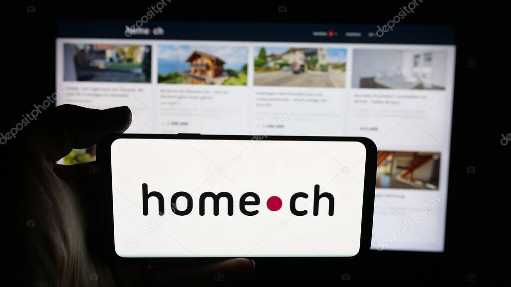 Stuttgart, Germany - 10-09-2025: Person holding cellphone with logo of Swiss real estate portal company Home.ch on screen in front of webpage. Focus on phone display.