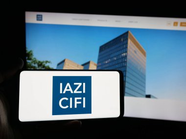 Stuttgart, Almanya - 10-10-2025: İnternet sitesi önünde üzerinde emlak hizmetleri şirketi IAZI AG 'nin (CIFI SA) logosu bulunan akıllı telefon sahibi kişi. Telefon ekranına odaklan.
