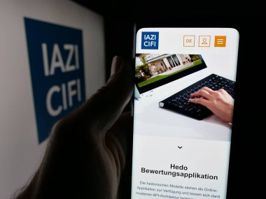 Stuttgart, Almanya - 10-10-2025: Emlak hizmetleri şirketi IAZI AG 'nin (CIFI SA) web sayfası ile akıllı telefon sahibi kişi logonun önünde ekranda. Telefon ekranının merkezine odaklan.
