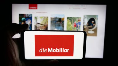 Stuttgart, Almanya - 10-10-2025: Cep telefonunda İsviçreli sigorta şirketi Mobiliar 'ın logosu olan kişi web sayfasının önünde ekranda. Telefon ekranına odaklan.