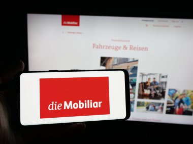 Stuttgart, Almanya - 10-10-2025: İsviçreli sigorta şirketi Mobiliar 'ın logosunu elinde tutan kişi web sitesinin önünde ekranda. Telefon ekranına odaklan.