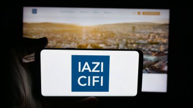 Stuttgart, Almanya - 10-10-2025: İnternet sayfası önünde üzerinde emlak hizmetleri şirketi IAZI AG 'nin (CIFI SA) logosu bulunan kişi. Telefon ekranına odaklan.
