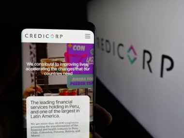 Stuttgart, Almanya - 10-11-2025: Peru 'lu finans şirketi Credicorp' un internet sayfası ile logo önünde cep telefonu tutan kişi. Telefon ekranının merkezine odaklan.