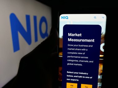 Stuttgart, Almanya - 10-11-2025: Araştırma şirketi Nielsen Consumer LLLC 'nin (NIQ) web sitesi ile akıllı telefon sahibi kişi logo önünde ekranda. Telefon ekranının merkezine odaklan.