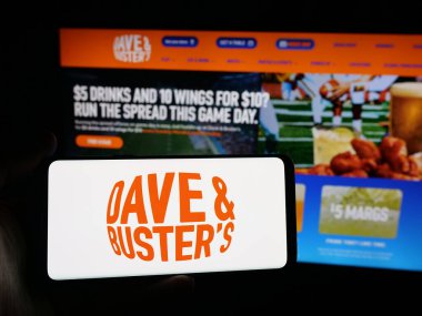 Stuttgart, Almanya - 10-13-2025: Dave and Buster 's Entertainment Inc. şirketinin logosunu elinde tutan kişi web sitesinin önünde ekranda. Telefon ekranına odaklan.
