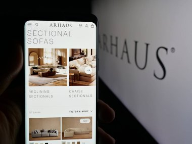 Stuttgart, Almanya - 10-13-2025: ABD 'li mobilya şirketi Arhaus Inc.' in web sayfası ile cep telefonu tutan kişi logonun önünde ekranda. Telefon ekranının merkezine odaklan.