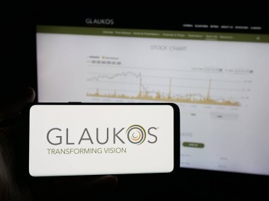 Stuttgart, Almanya - 10-13-2025: İnternet sitesi önünde ekranda ABD 'li oftalmik şirket Glaukos Corporation' ın logosuna sahip akıllı telefonu tutan kişi. Telefon ekranına odaklan.