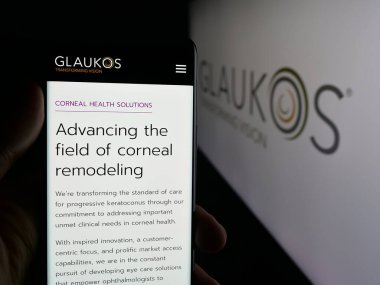 Stuttgart, Almanya - 10-13-2025: ABD 'li oftalmik şirketi Glaukos Corporation' ın web sayfası olan akıllı telefon sahibi kişi logonun önünde ekranda. Telefon ekranının merkezine odaklan.