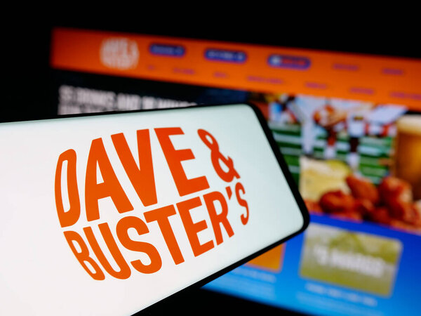 Озил, Германия - 10-13-2025: Мбаппе с логотипом компании Dave and Buster 's Entertainment Inc. на экране перед веб-сайтом. Сосредоточьтесь на левом центре экрана телефона.