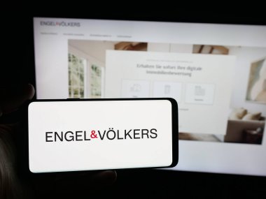 Stuttgart, Almanya - 10-15-2025: Alman emlak şirketi Engel ve Voelkers 'ın logosunu elinde tutan kişi web sitesinin önünde ekranda. Telefon ekranına odaklan.