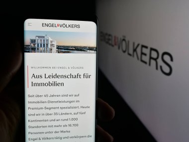 Stuttgart, Almanya - 10-15-2025: Alman emlak şirketi Engel ve Voelkers 'ın internet sayfası logonun önünde duran kişi. Telefon ekranının merkezine odaklan.