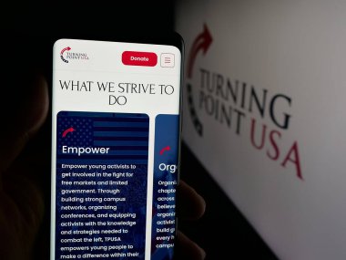 Stuttgart, Almanya - 10-15-2025: ABD 'nin Turning Point USA (TPUSA) adlı organizasyonunun web sayfası logo önünde bulunan kişi. Telefon ekranının merkezine odaklan.