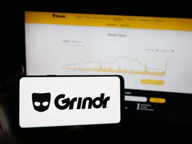 Stuttgart, Almanya - 10-15-2025: İnternet sitesi önünde ekranda LGBT sosyal medya platformu şirketi Grindr Inc 'in logosuna sahip akıllı telefonu tutan kişi. Telefon ekranına odaklan.