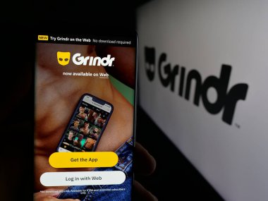 Stuttgart, Almanya - 10-15-2025: Logo önünde ekranda LGBT sosyal medya platformu şirketi Grindr Inc 'in web sayfası ile akıllı telefon tutan kişi. Telefon ekranının merkezine odaklan.