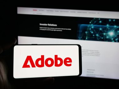 Stuttgart, Almanya - 10-16-2025: ABD 'li yazılım şirketi Adobe Inc.' in logosuyla akıllı telefon sahibi kişi web sitesinin önünde ekranda. Telefon ekranına odaklan.