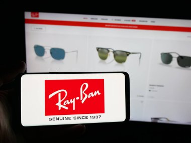 Stuttgart, Almanya - 10-16-2025: Lüks gözlük şirketi Ray-Ban 'in logosuna sahip akıllı telefon sahibi kişi web sitesinin önünde ekranda. Telefon ekranına odaklan.