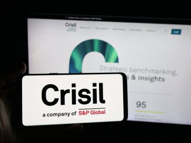 Stuttgart, Almanya - 10-16-2025: Hintli derecelendirme şirketi CRISIL Limited 'in logosuna sahip akıllı telefon sahibi kişi web sitesinin önünde ekranda. Telefon ekranına odaklan.
