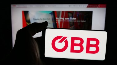 Stuttgart, Almanya - 10-17-2025: Üzerinde demiryolu şirketi Oesterreichische Bundesbahnen 'in logosu olan cep telefonu sahibi kişi web sayfasının önünde ekranda. Telefon ekranına odaklan.