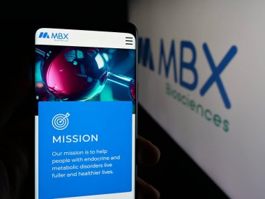 Stuttgart, Almanya - 10-18-2025: ABD 'li biyofizik şirketi MBX Biyobilim Şirketi' nin web sayfası olan akıllı telefon sahibi kişi logonun önünde ekranda. Telefon ekranının merkezine odaklan.