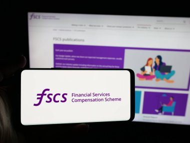 Stuttgart, Almanya - 10-18-2025: İnternet sitesi önünde üzerinde Mali Hizmetler Telafi Şeması (FSCS) logosu bulunan akıllı telefon sahibi kişi. Telefon ekranına odaklan.