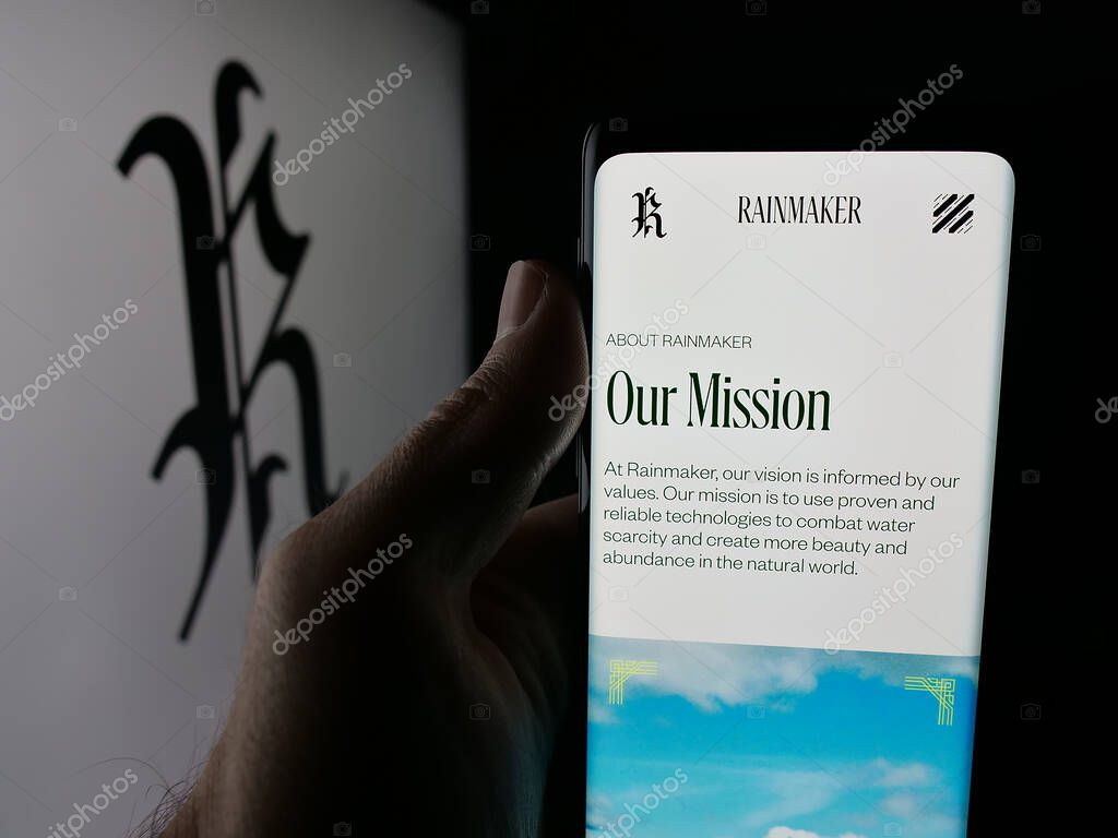 Stuttgart, Germany - 10-15-2025: Person holding smartphone with web page of cloud seeding company Rainmaker Technology on screen in front of logo. Focus on center of phone display.
