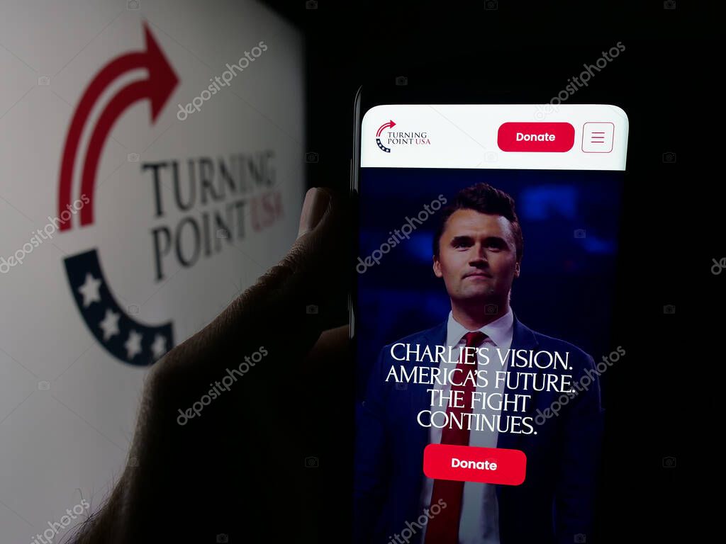 Stuttgart, Germany - 10-15-2025: Person holding smartphone with web page of US organisation Turning Point USA (TPUSA) on screen in front of logo. Focus on center of phone display.