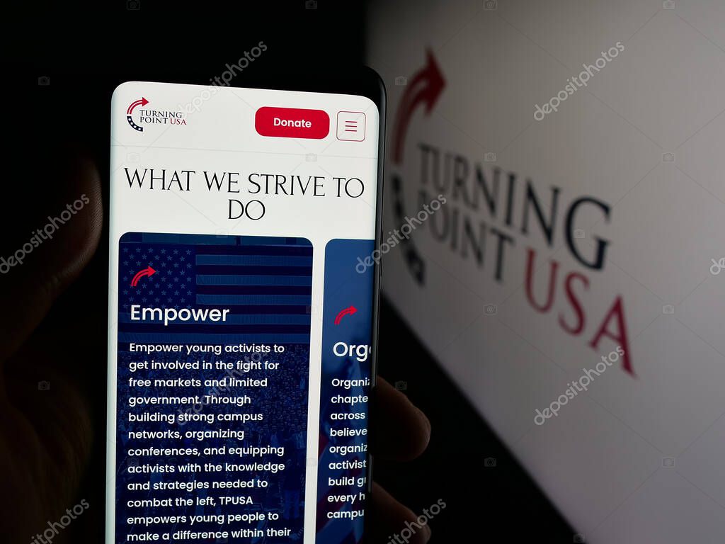 Stuttgart, Germany - 10-15-2025: Person holding cellphone with webpage of US organisation Turning Point USA (TPUSA) on screen in front of logo. Focus on center of phone display.