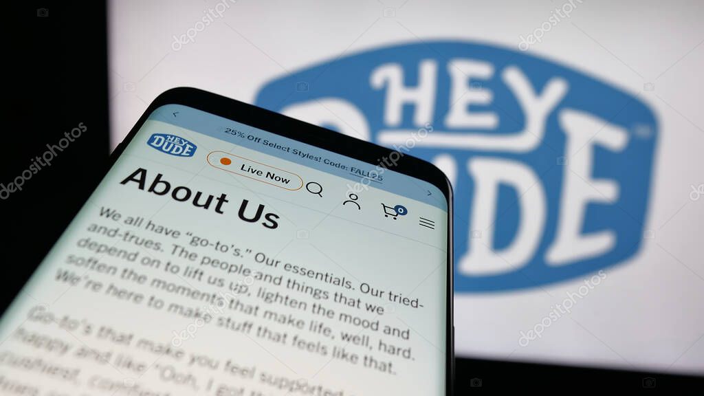 Stuttgart, Germany - 10-15-2025: Mobile phone with website of US fashion company Heydude (Heydude.com) on screen in front of logo. Focus on top-left of phone display.