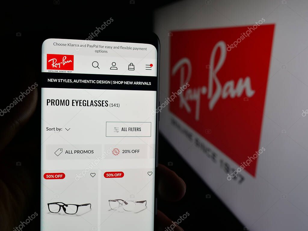 Stuttgart, Germany - 10-16-2025: Person holding smartphone with web page of luxury eyewear company Ray-Ban on screen in front of logo. Focus on center of phone display.