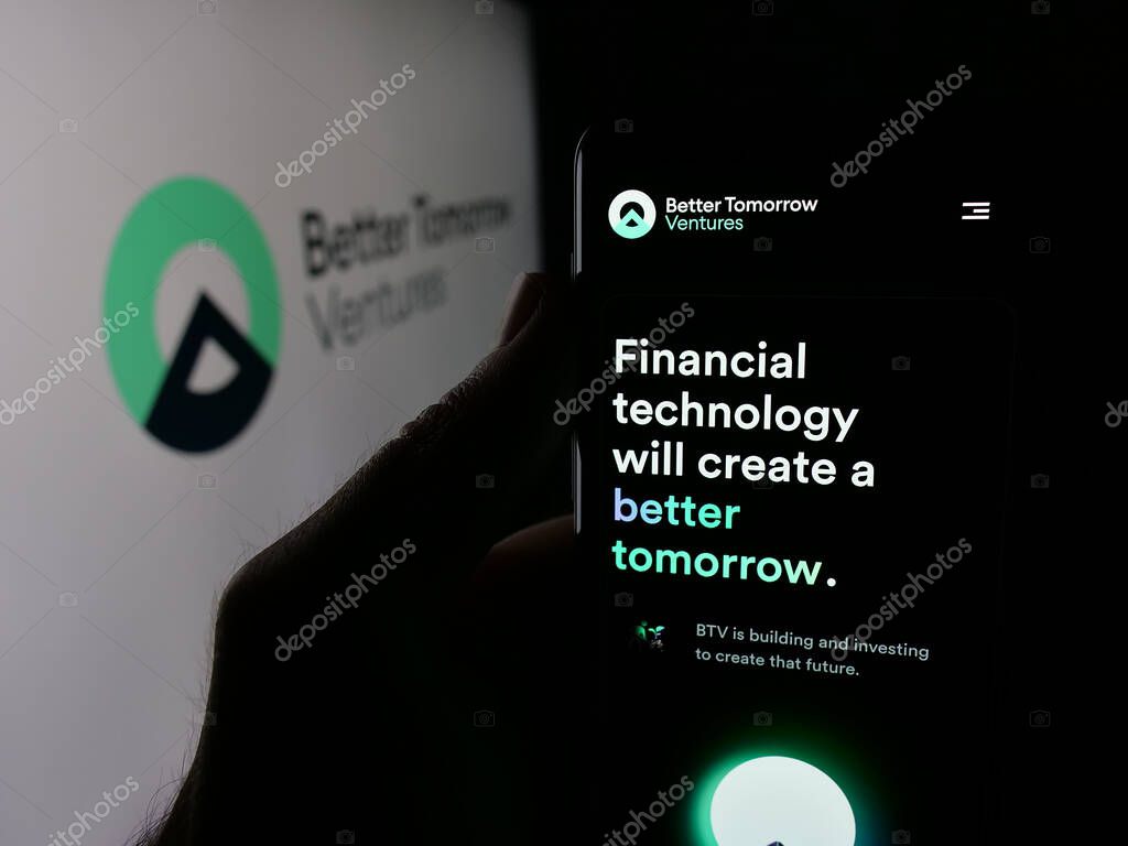 Stuttgart, Germany - 10-18-2025: Person holding smartphone with web page of US company Better Tomorrow Ventures (BTV) on screen in front of logo. Focus on center of phone display.