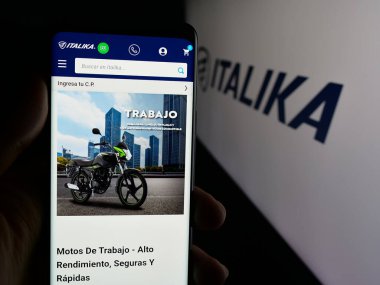 Stuttgart, Almanya - 10-20-2025: Meksikalı motosiklet şirketi Italika 'nın web sayfası ile logo önünde cep telefonu tutan kişi. Telefon ekranının merkezine odaklan.