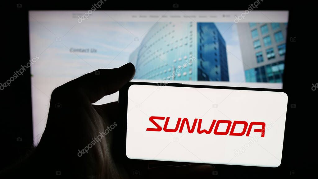 Stuttgart, Germany - 10-19-2025: Person holding mobile phone with logo of Chinese company Sunwoda Electronic Co. Ltd. on screen in front of web page. Focus on phone display.