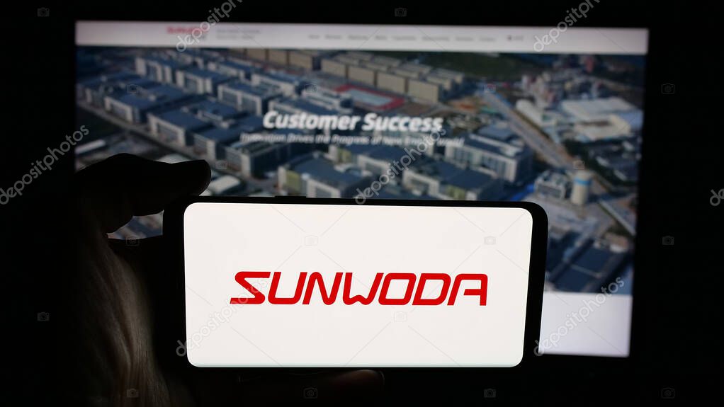 Stuttgart, Germany - 10-19-2025: Person holding cellphone with logo of Chinese company Sunwoda Electronic Co. Ltd. on screen in front of webpage. Focus on phone display.