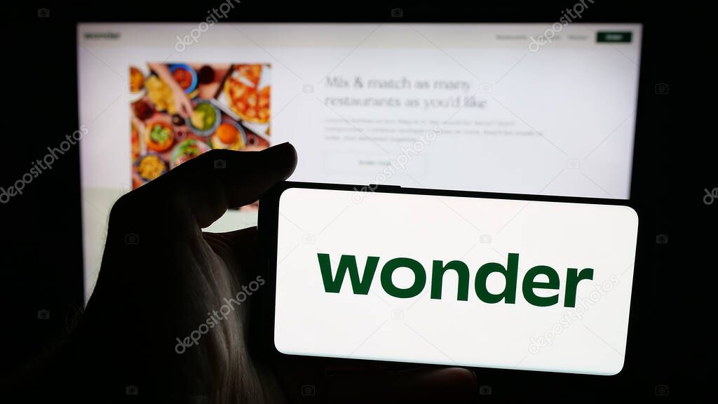 Stuttgart, Germany - 10-20-2025: Person holding mobile phone with logo of US food delivery company Wonder Group Inc. on screen in front of web page. Focus on phone display.
