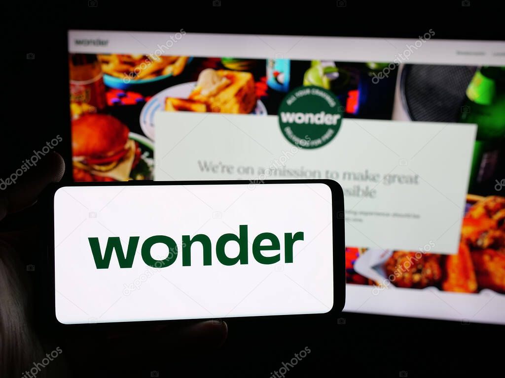 Stuttgart, Germany - 10-20-2025: Person holding smartphone with logo of US food delivery company Wonder Group Inc. on screen in front of website. Focus on phone display.