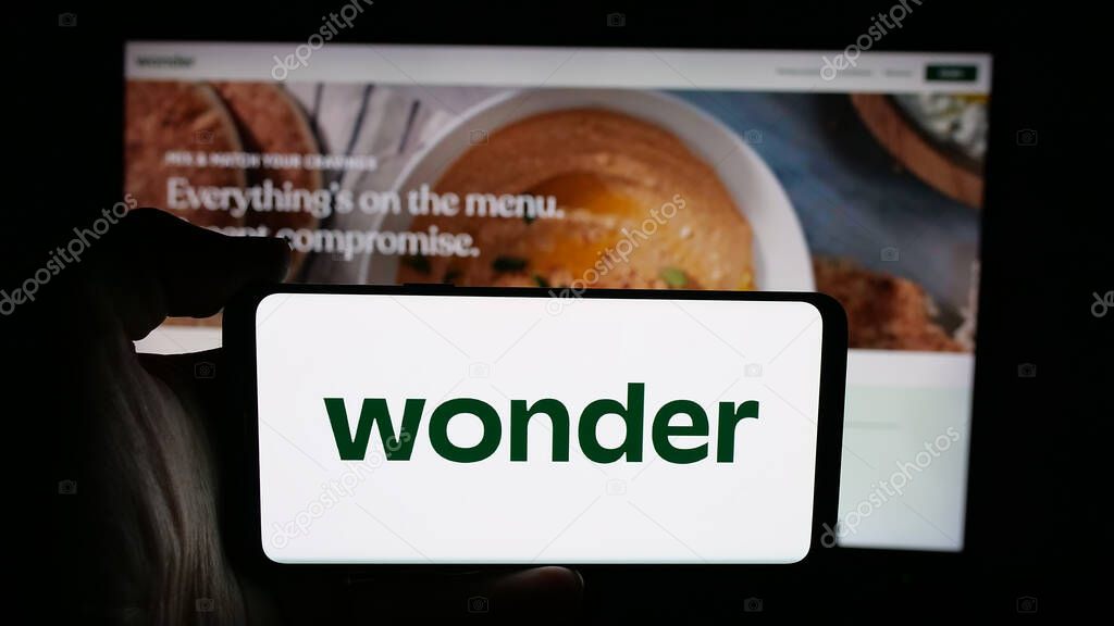 Stuttgart, Germany - 10-20-2025: Person holding cellphone with logo of US food delivery company Wonder Group Inc. on screen in front of webpage. Focus on phone display.