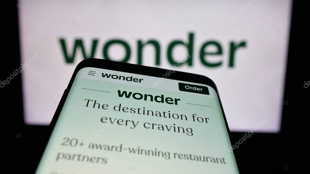 Stuttgart, Germany - 10-20-2025: Mobile phone with website of US food delivery company Wonder Group Inc. on screen in front of logo. Focus on top-left of phone display.