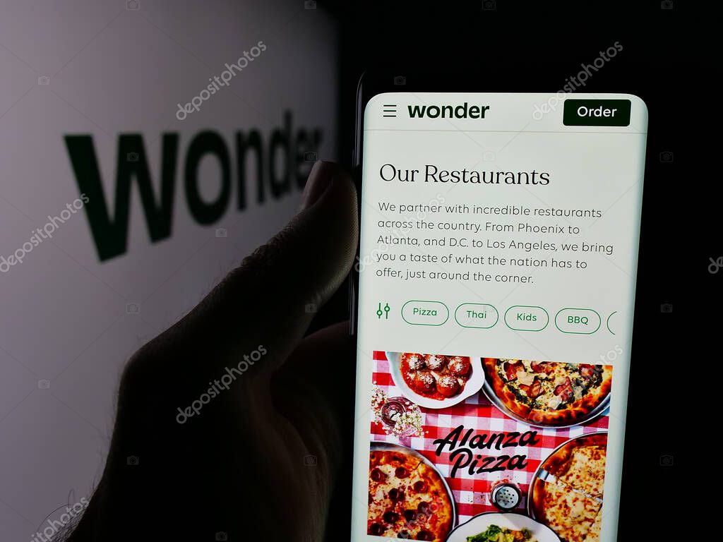 Stuttgart, Germany - 10-20-2025: Person holding smartphone with web page of US food delivery company Wonder Group Inc. on screen in front of logo. Focus on center of phone display.