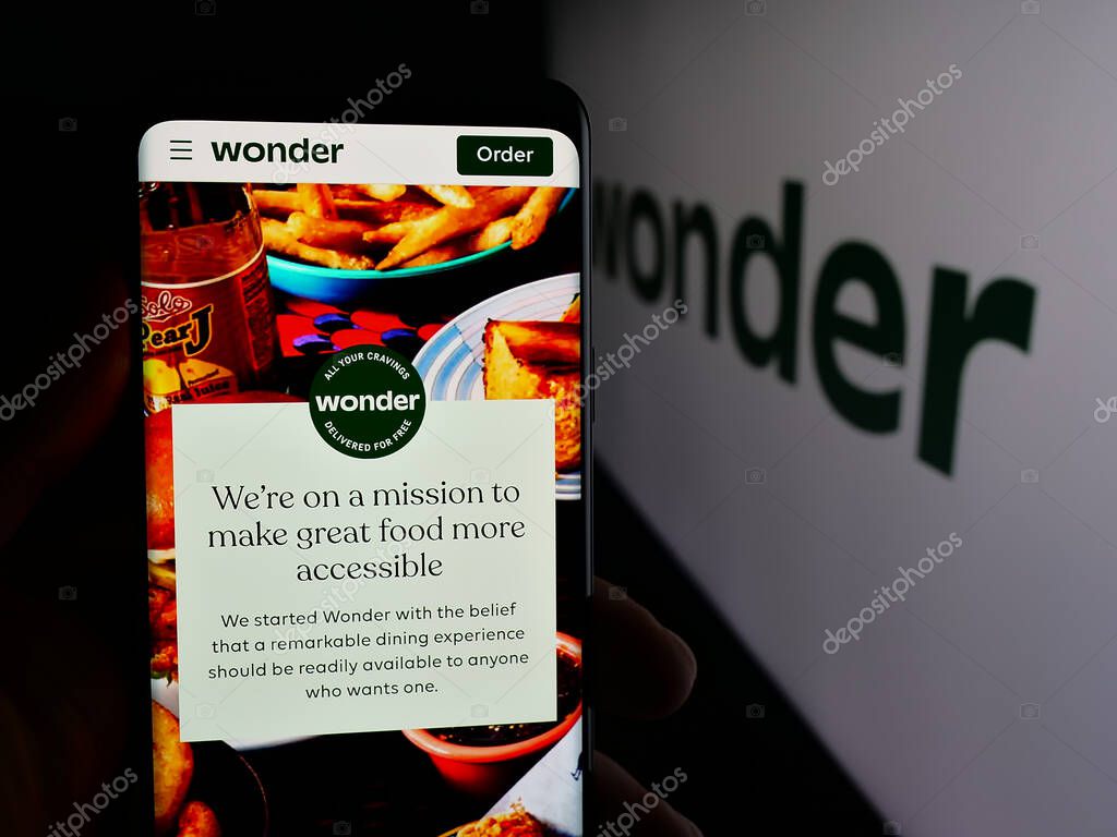 Stuttgart, Germany - 10-20-2025: Person holding cellphone with webpage of US food delivery company Wonder Group Inc. on screen in front of logo. Focus on center of phone display.