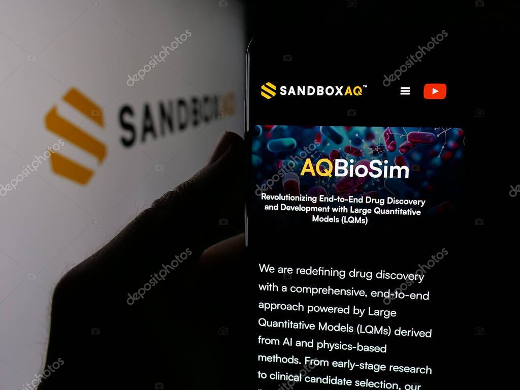 Stuttgart, Germany - 10-20-2025: Person holding cellphone with webpage of US company SB Technology Inc. (SandboxAQ) on screen in front of logo. Focus on center of phone display.