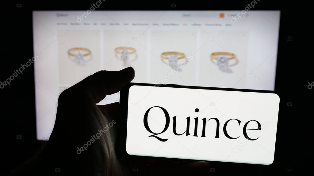 Stuttgart, Germany - 10-20-2025: Person holding mobile phone with logo of US fashion company Last Brand Inc. (Quince) on screen in front of web page. Focus on phone display.