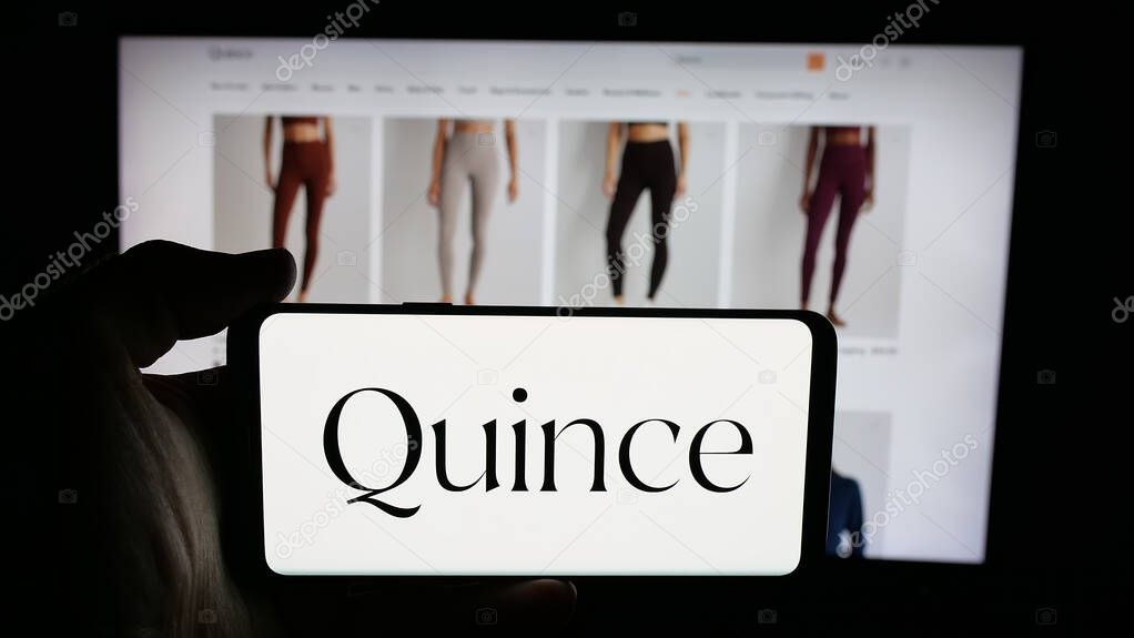 Stuttgart, Germany - 10-20-2025: Person holding cellphone with logo of US fashion company Last Brand Inc. (Quince) on screen in front of webpage. Focus on phone display.